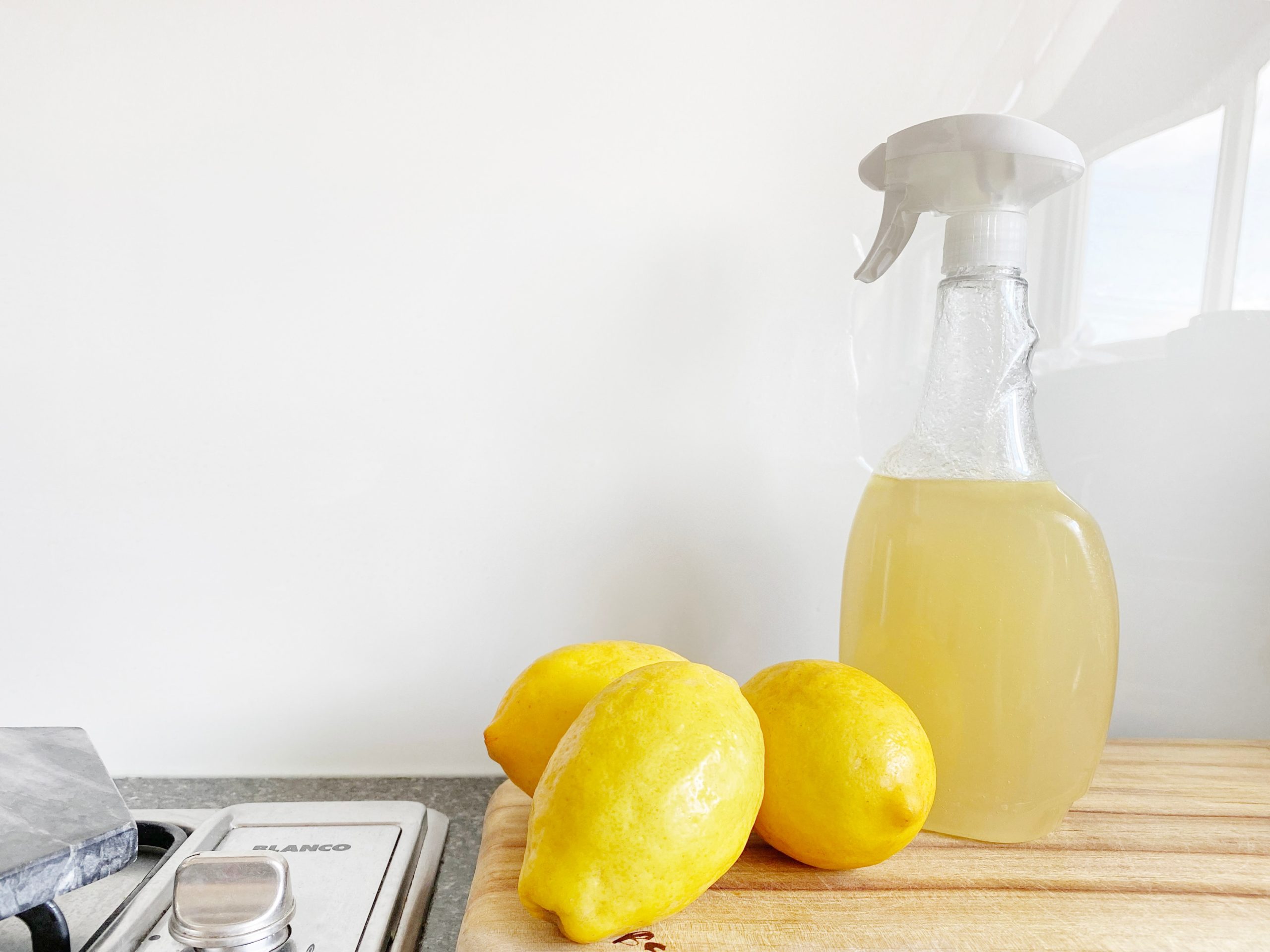 Three lemons and a bottle of cleaning solution sitting on a kitchen counter