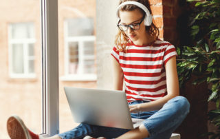 Calm young woman in headphones listening to music and working on laptop at home