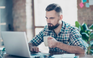 Concept of having a break at work. Concentrated calm peaceful serious office worker watching carefully a video on the internet using his laptop and drinking tea