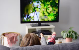 A young woman from behind watching TV while sitting on sofa in living room